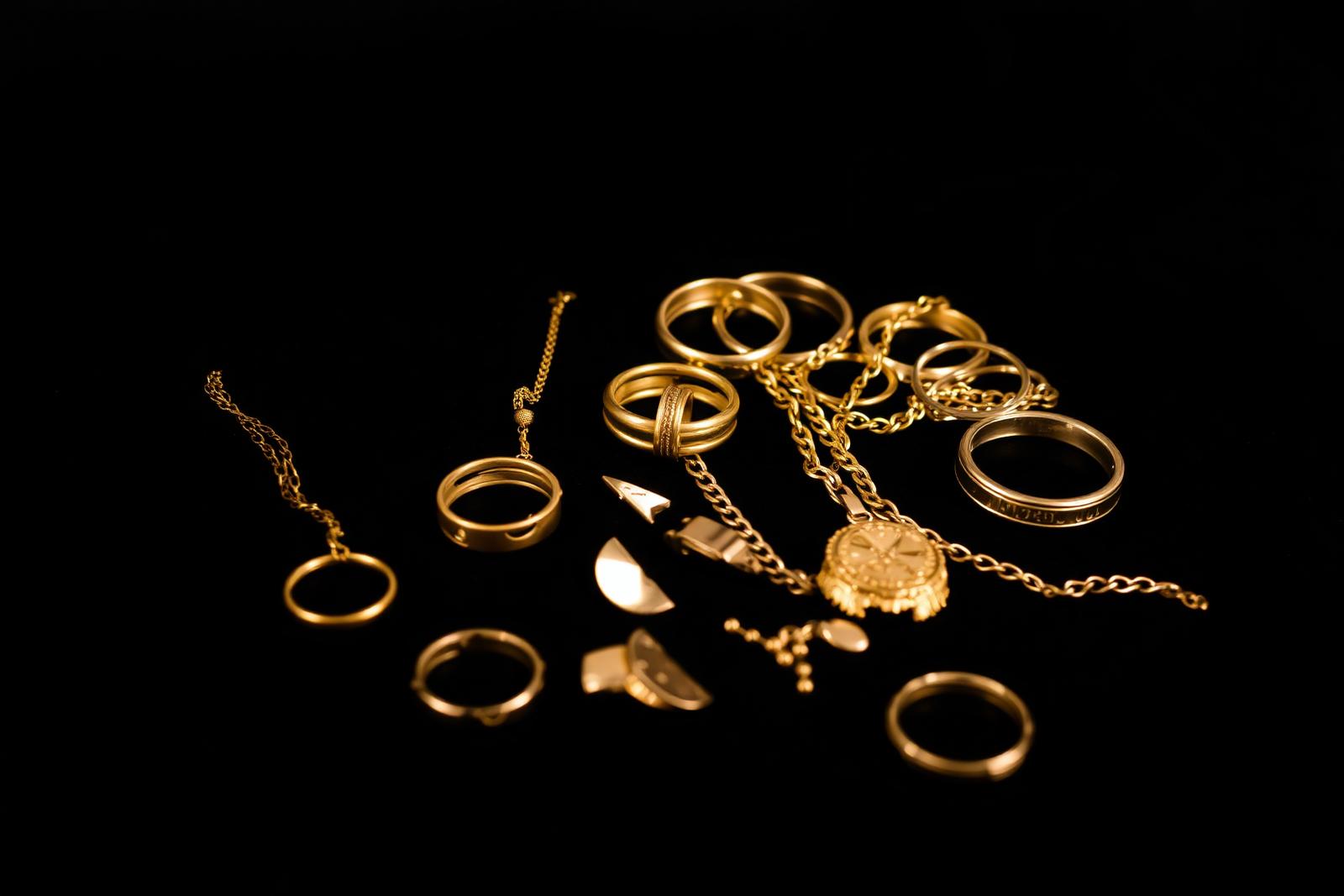 Assorted gold jewellery — rings, chains, broken pieces — on a dark surface